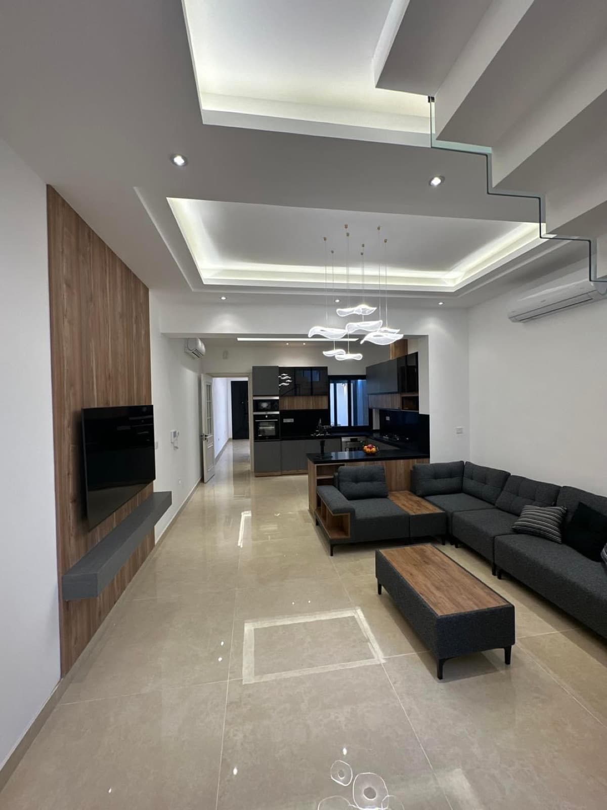 Open-plan living space with a sectional sofa, glass-balustrade staircase, and kitchen