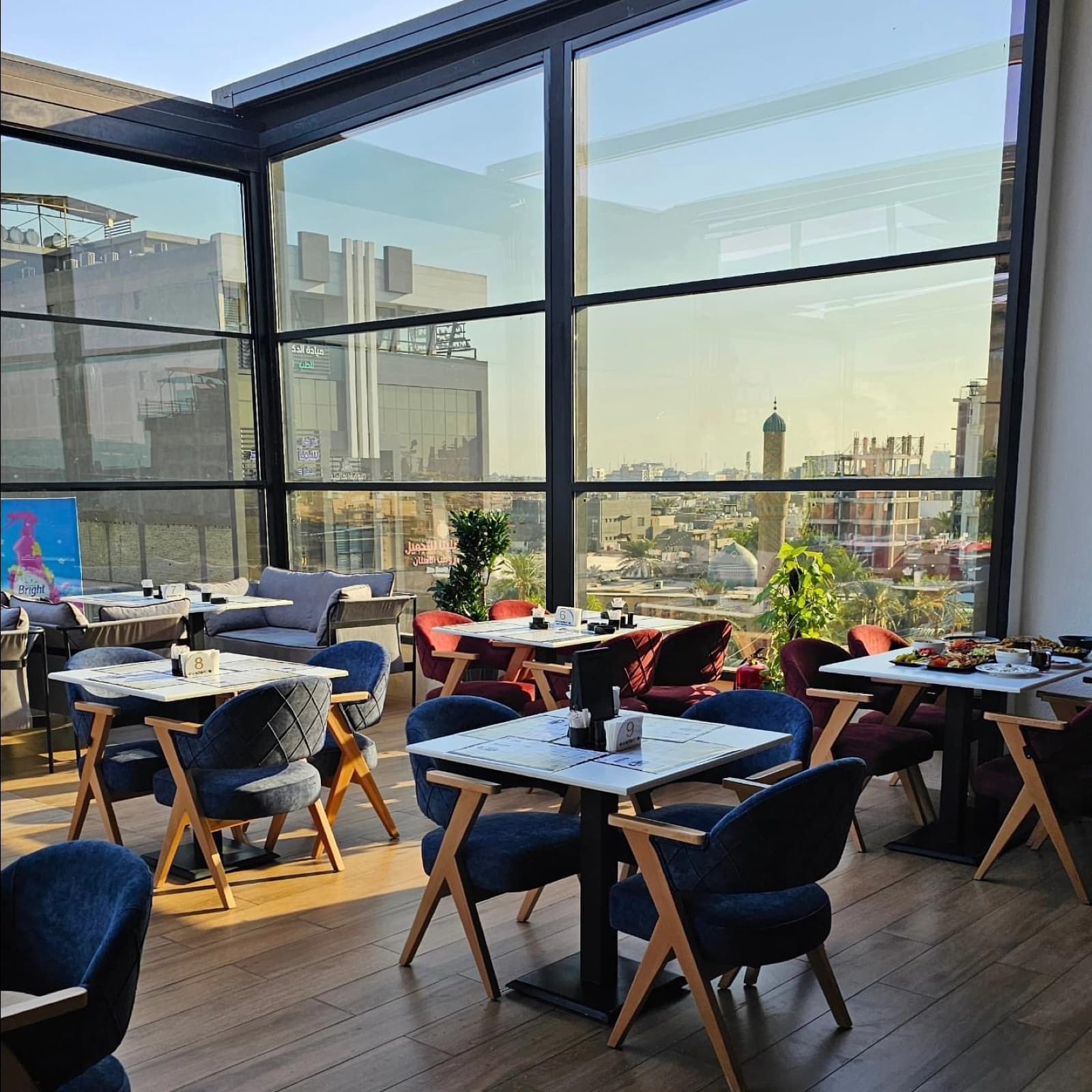 Dining interior with blue and red seating beside floor-to-ceiling windows overlooking the city