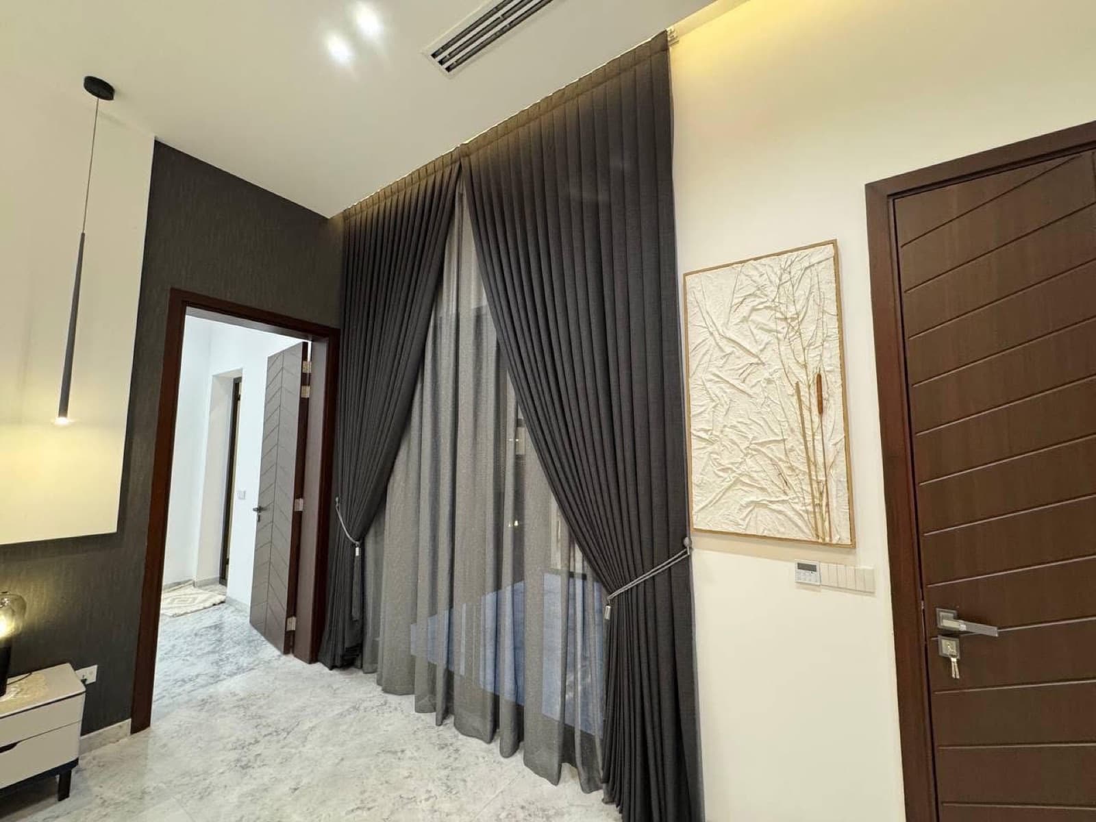 Bedroom corner with tall dark curtains, dark wood doors, and pale stone flooring