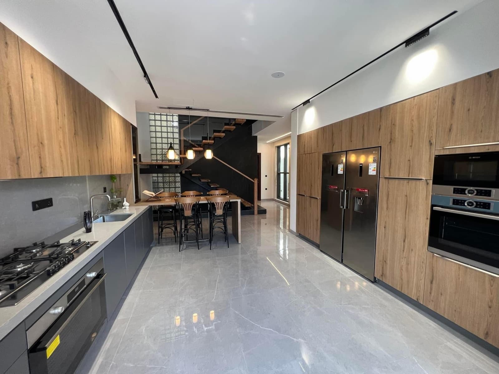 Kitchen with wood cabinetry, grey counters, black appliances, and an open staircase