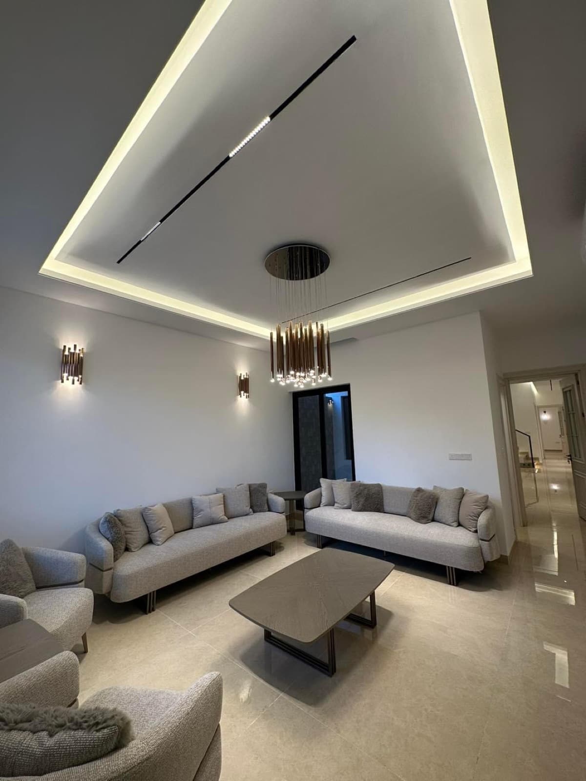 Living room with pale upholstered seating, concealed ceiling lighting, and a pendant fixture
