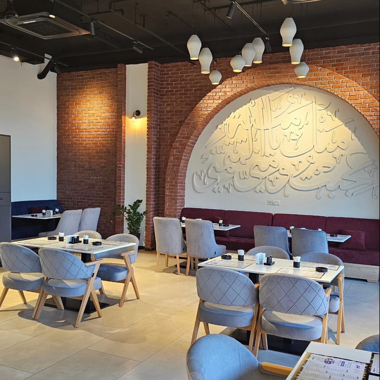 Restaurant interior with a brick arch, Arabic calligraphy relief, and grey and red seating
