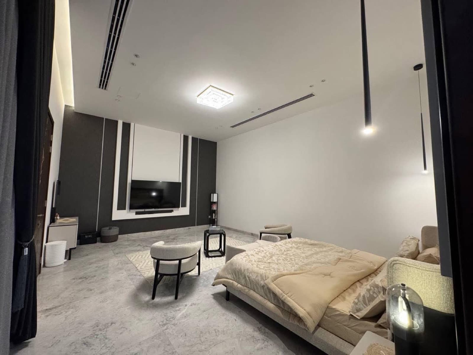 Bedroom with black and white wall panels, a bed, lounge seating, and a wall-mounted television