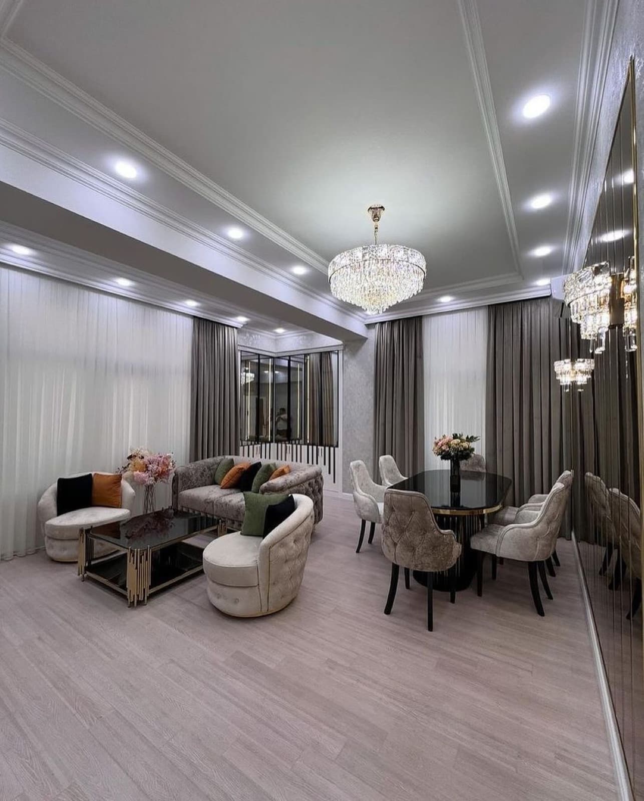 Combined living and dining room with chandeliers, grey curtains, and a mirrored wall