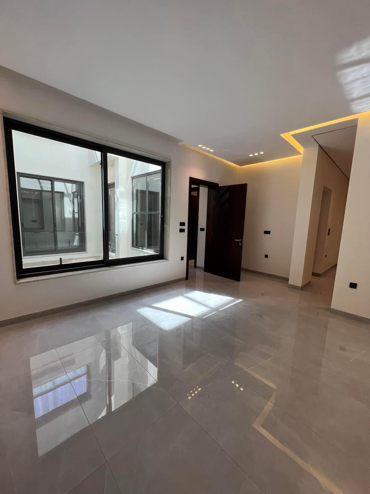 Bright room with reflective grey flooring, dark-framed courtyard windows, and concealed ceiling lighting