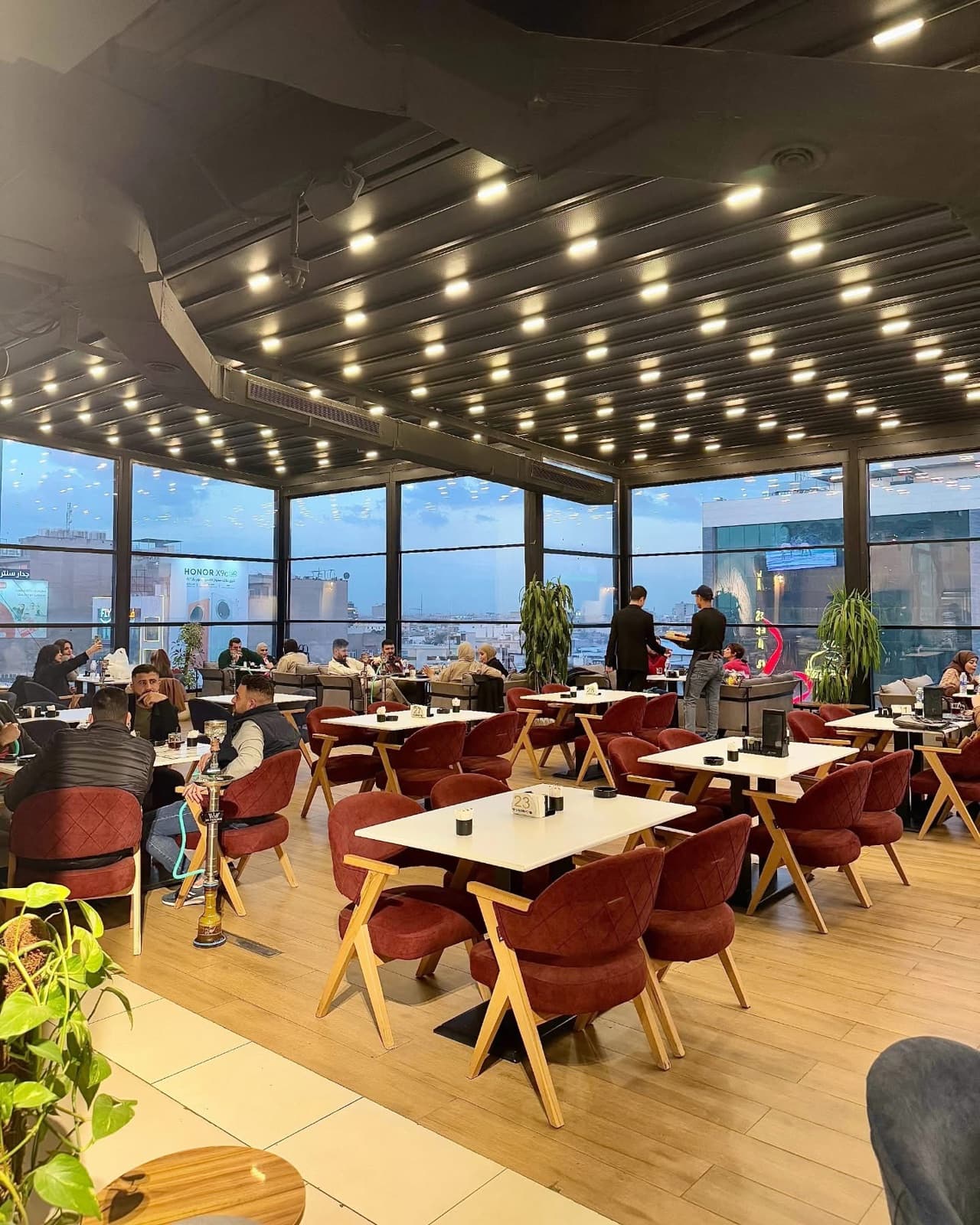 Occupied restaurant interior with red seating, a black ceiling, and broad city-facing glazing
